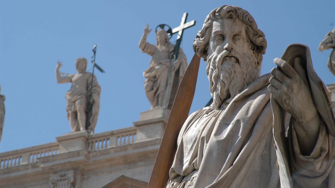 Figur des heiligen Paulus auf dem Petersplatz in Rom (im Hintergrund Christus mit dem Kreuz auf der Fassade des Petersdoms).