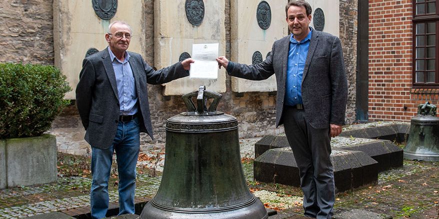 Hans Manek (links) und Prof. Dr. Thomas Flammer vor der Glocke, die im Innenhof des Kirchengerichts steht.