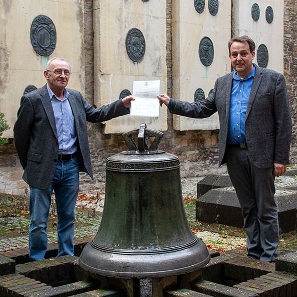 Hans Manek (links) und Prof. Dr. Thomas Flammer vor der Glocke, die im Innenhof des Kirchengerichts steht.